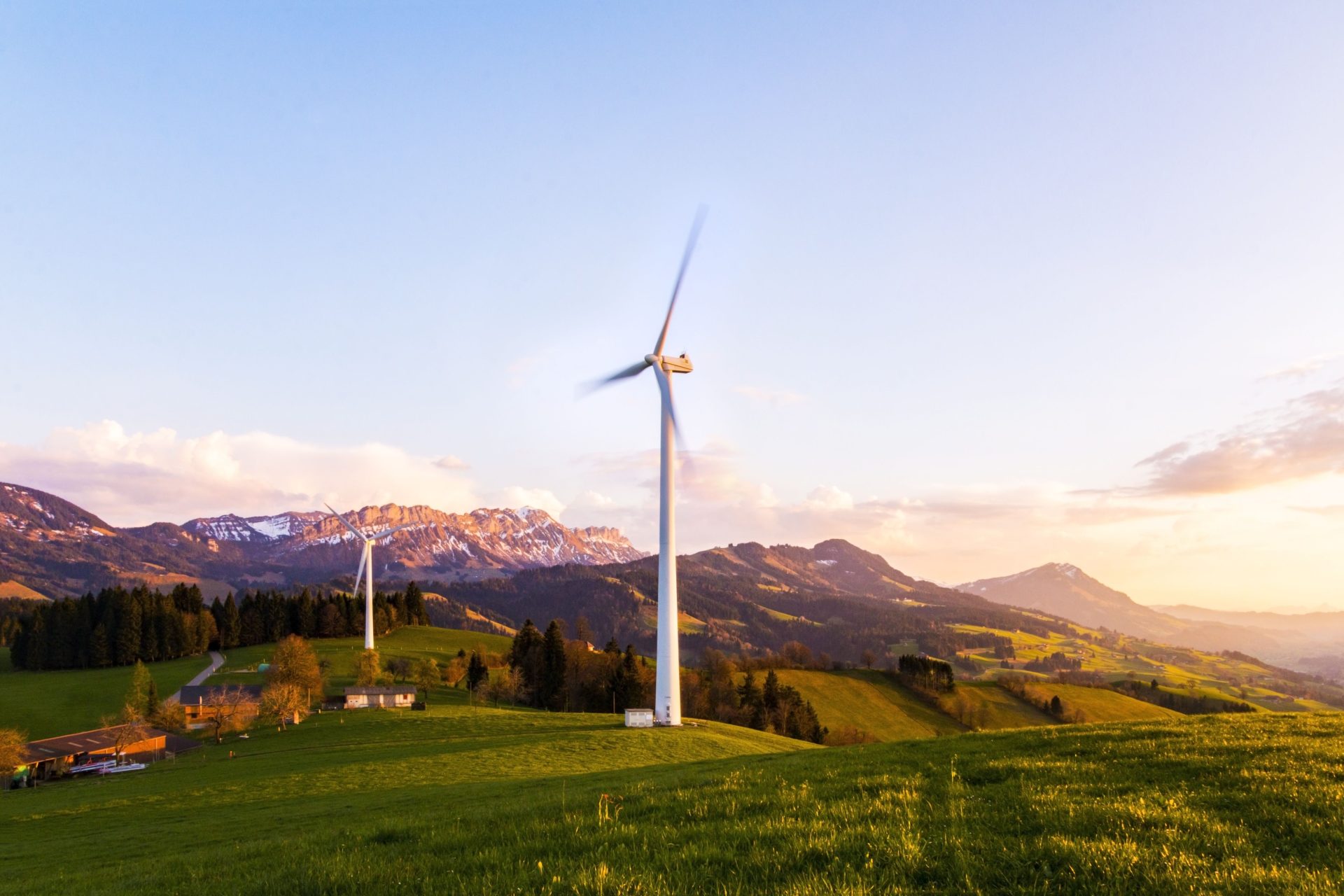 Eine Windkraftanlage ragt vor einer bergigen Kulisse unter einem farbenprächtigen Himmel bei Sonnenuntergang empor.